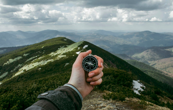 A person holding a silver compass in front of a misty mountain range