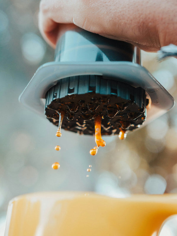 A camper brewing fresh coffee outdoors, with coffee dripping into a cup