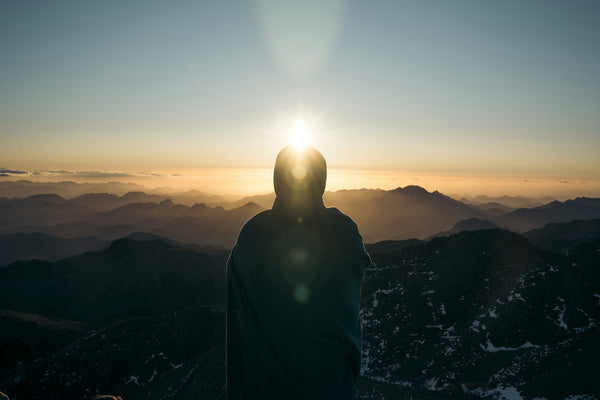 A hiker in a jacket standing on a mountain ridge at sunrise
