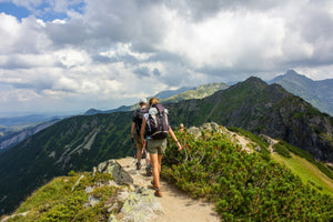 A hiker walking a sun-baked dirt trail through open mountain country on a clear summer day