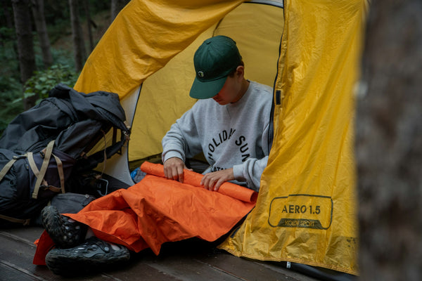 A camper inside a tent rolling up a sleeping pad on a cool morning in the mountains