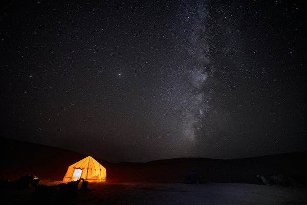 A tent glowing beneath the Milky Way and a sky full of stars at a remote campsite
