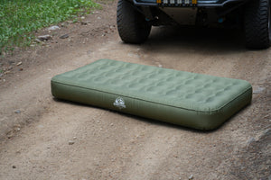 Durable 40D nylon Basecamp Mattress lying directly on rough dirt trail in front of an off-road truck